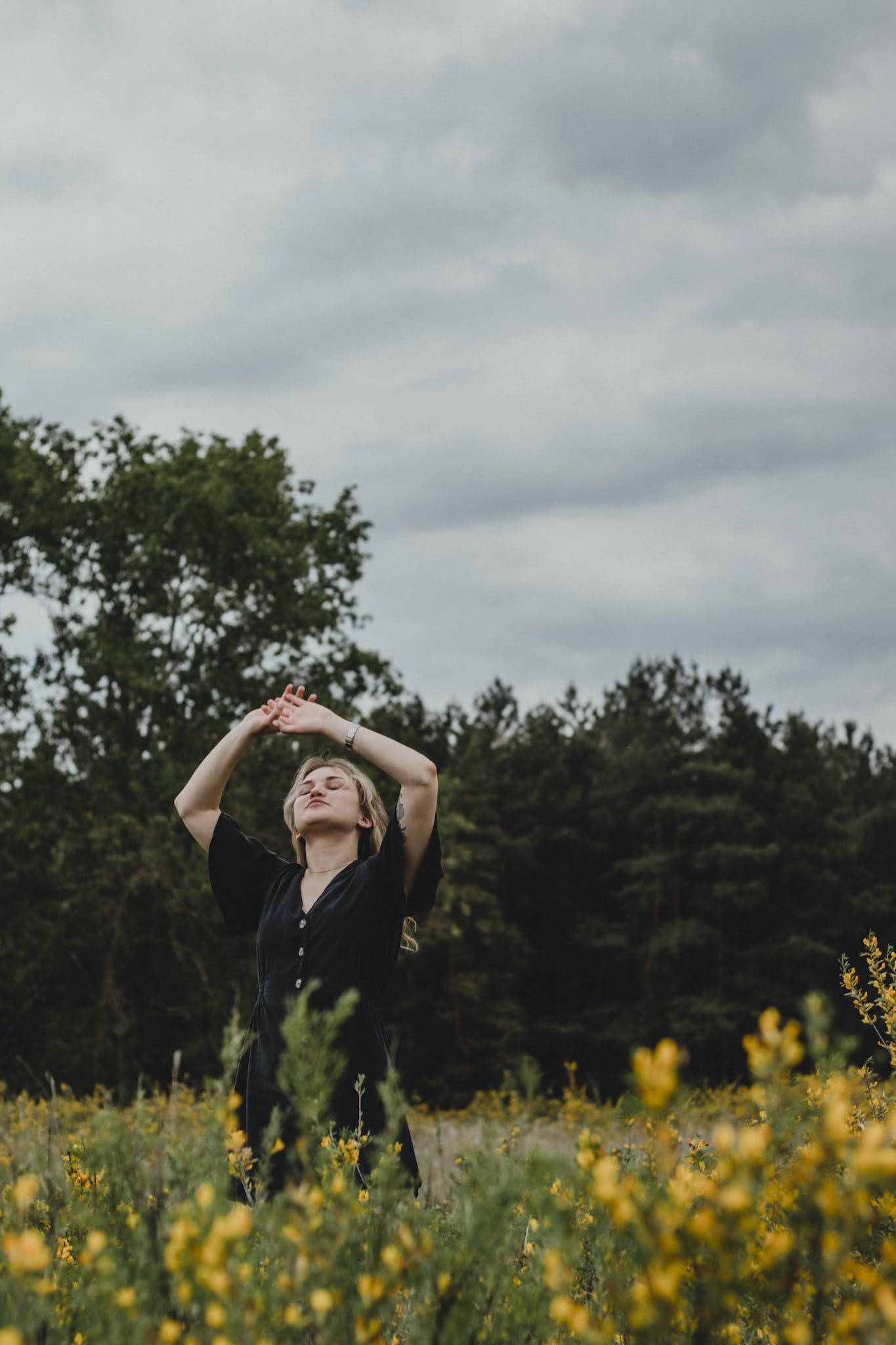 A woman in a black dress is standing in a field of yellow flowers