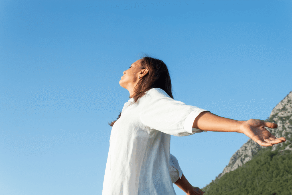 Femme en pleine inspiration, les bras ouverts, respirant profondément dans la nature.