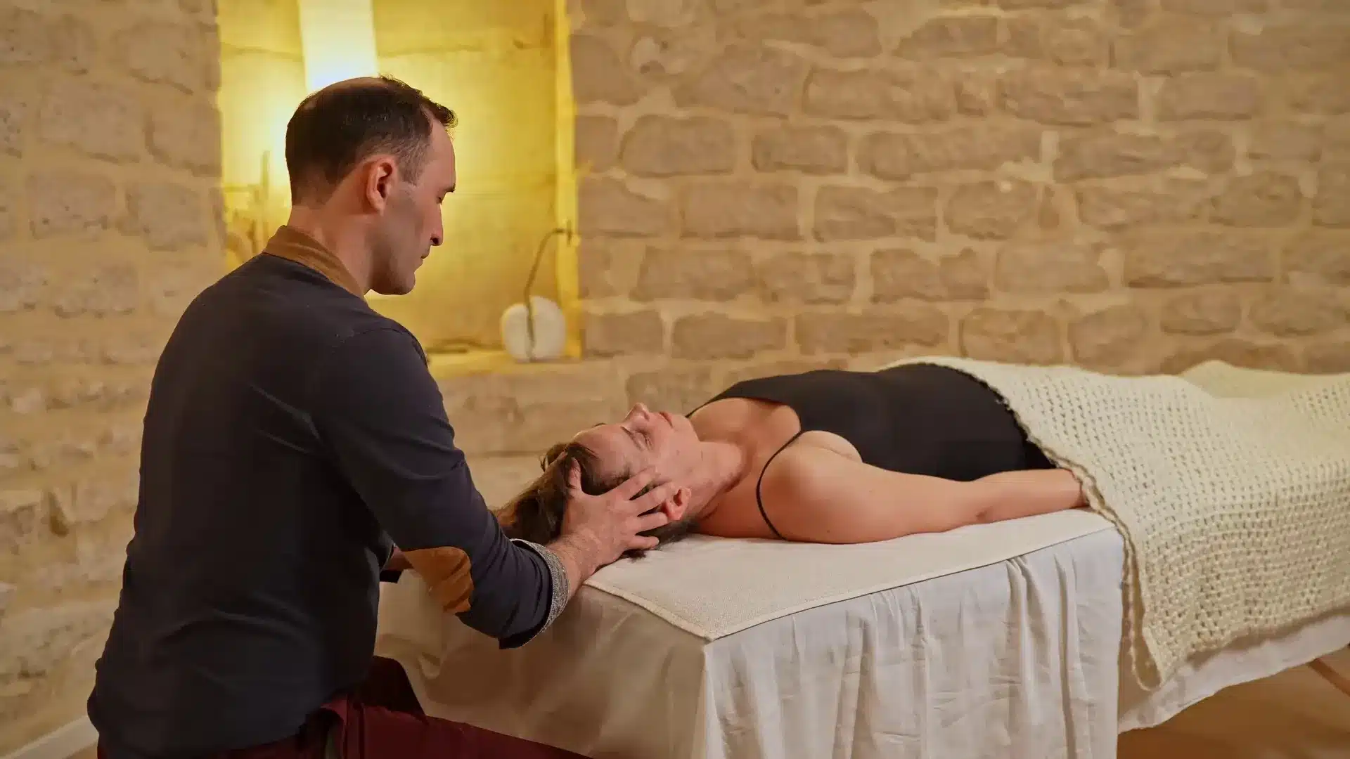 Le fasciathérapeute accompagne la nuque d'une patiente allongée