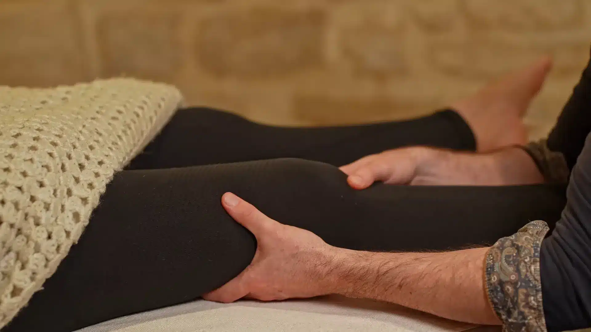 Mains du praticien posées sur la cuisse et le genou d'une patiente allongée